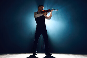 Lost in melody. Violinist in formal wear playing with passion on stage with dramatic smoke lit by...