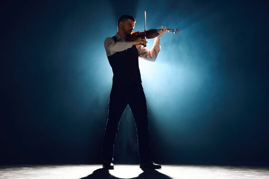 Lost in melody. Violinist in formal wear playing with passion on stage with dramatic smoke lit by backlight. Concept of instrumental music festivals and concerts, art, culture. Ad