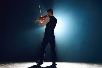 Professional musician with violin under performing his new melody on stage with spotlights...