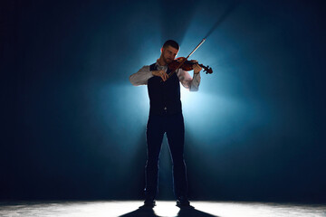Intense violin recital with musician standing on stage with backlights against darkness with smoke....