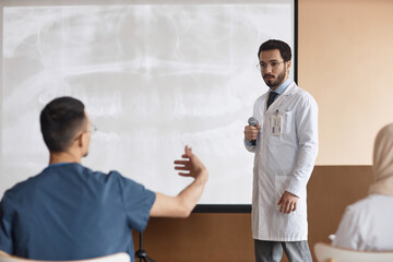 Middle Eastern man with microphone listening to unrecognizable male conference participants...