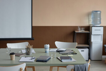 Part of office interior with focus on messy desk with papers, stationery, coffee cups and water glasses on top left by workers after meeting