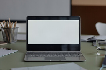 Close up shot of modern operating laptop with blank white screen and stationery on table in meeting room
