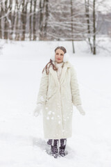 Happy young woman in a white fur coat, mittens and fur headphones on a winter walk in the park