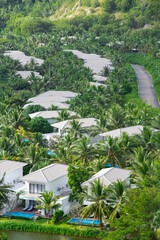 Fototapeta na wymiar Aerial view riverside white painted tropical villas swimming pool, lounge chairs surrounding lush green coconut palm trees, row upscale two story vacation home roof tiles, luxury neighborhood