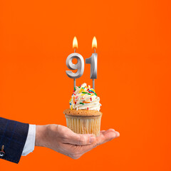 The hand that delivers cupcake with the number 91 candle - Birthday on orange background