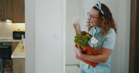Female caregiver enters in apartman and brings a paper bag of groceries for senior woman in wheelchair while helping and care her home