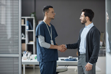 Side view of Muslim man physical therapist and male patient thanking each other with handshake...