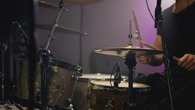 a young attractive guy plays a drum kit. Strikes a cymbal, rehearses. Performance of a rock band, hobby. A man is learning music. Male professional holds drumsticks in hands. Drum set in slow motion