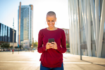 smiling woman holding and looking at phone in the city