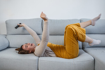Happy woman lying on her back on the sofa with a smart phone in her hand