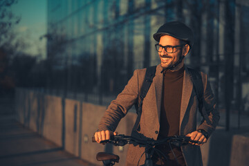 A happy young adult businessman pushing his bicycle on his way home from work