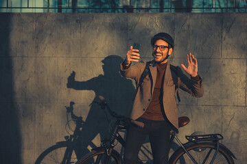 A happy adult male employee having a video call while gesticulating and leaning on a bicycle