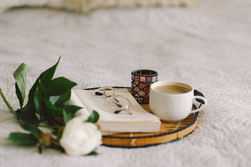 Still life details in home interior of living room. Open book with glasses, cup coffee and bouquet white pink peonies flowers. Read and rest. Cozy home