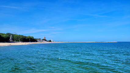 Blue sea and blue sky. in the background there is a city with a lighthouse and a Ferris wheel ending with a pier.