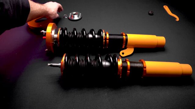 tuning car suspension, coilovers, shock absorbers and front springs in yellow and gold color for a sports drift car on a dark background assembly by the hands of a car mechanic
