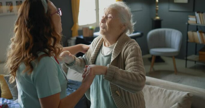 The caregiver motivates and helps the old woman to get up and walk