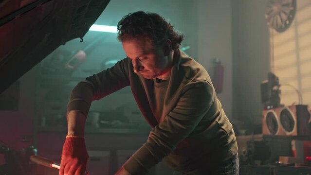 Auto mechanic working on car engine in mechanics garage. Repairman in gloves using wrench to repair auto engine. Repair service. Vehicle engine with dim red car light. Overheating of car engine.
