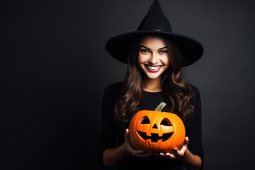 Smiling woman in witch hat holding pumpkin, dark background