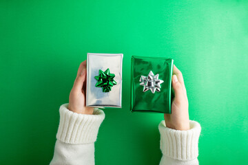 Dive into holiday magic! First person top view of hands reach for lavish green and silver giftbox featuring bow, on green backdrop. Perfect for mother day.
