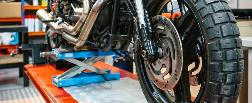 Banner of front wheel tyre and brake disk of custom motorbike on workshop. Front view of vintage scrambler motorcycle over platform ready to repair on mechanic garage.