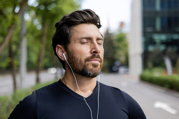 Close-up photo of a young male athlete wearing headphones and black sportswear standing outside on...