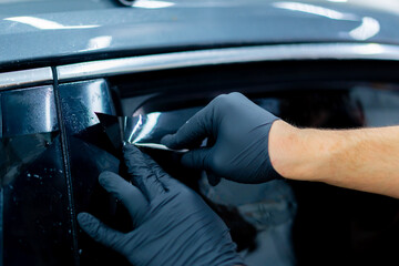 close-up repairman smooths the protective film for tinting on the car glass with a scraper detailing
