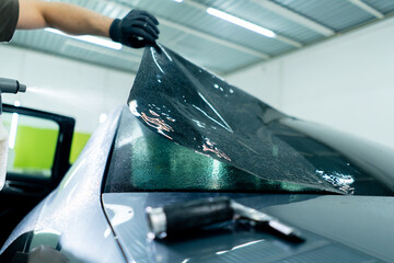 close-up of a car mechanic carefully sticking a protective tinted film on a car glass detailing