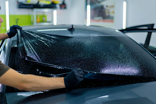 close-up of a car mechanic carefully sticking a protective tinted film on a car glass detailing