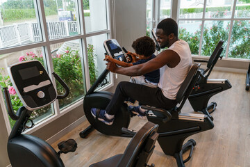 Father and son sitting on father's lap On the exercise bike in the gym joyfully