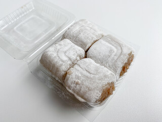 Moaci or Mochi covered in white flour. Rice cake filled with sweet peanut paste. In a plastic container. Isolated in white background