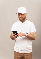 Vertical shot of a young bearded man wearing white delivery uniform holding a phone.