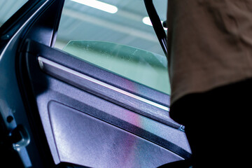 close-up of a car mechanic carefully sticking a protective tinted film on a car glass detailing