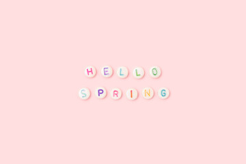 Hello spring. Quote made of white round beads with colorful letters on a pink background.