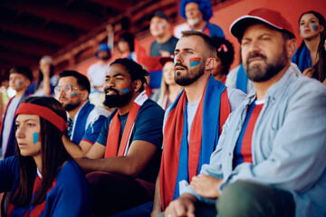 Group of male friends spectating sports game from stadium stands.