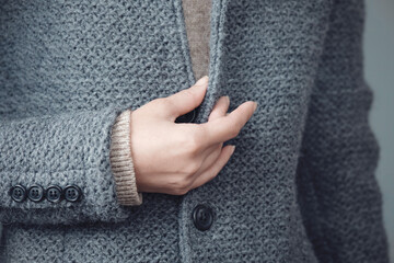 Close-up of a gray knitted jacket and a woman's hand. Winter, autumn warm woolen clothes.