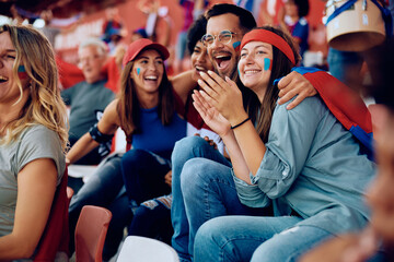 Multiracial group of cheerful friends celebrating during sports game at stadium.