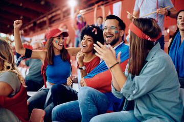 Group of sports fans having fun while cheering during match at stadium.