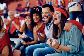 Group of cheerful sports fans celebrating during match at stadium.