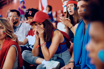 Young sports fan feeling sad after her team had lost match at stadium.