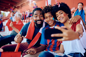 Happy black family taking selfie with cell phone at stadium.