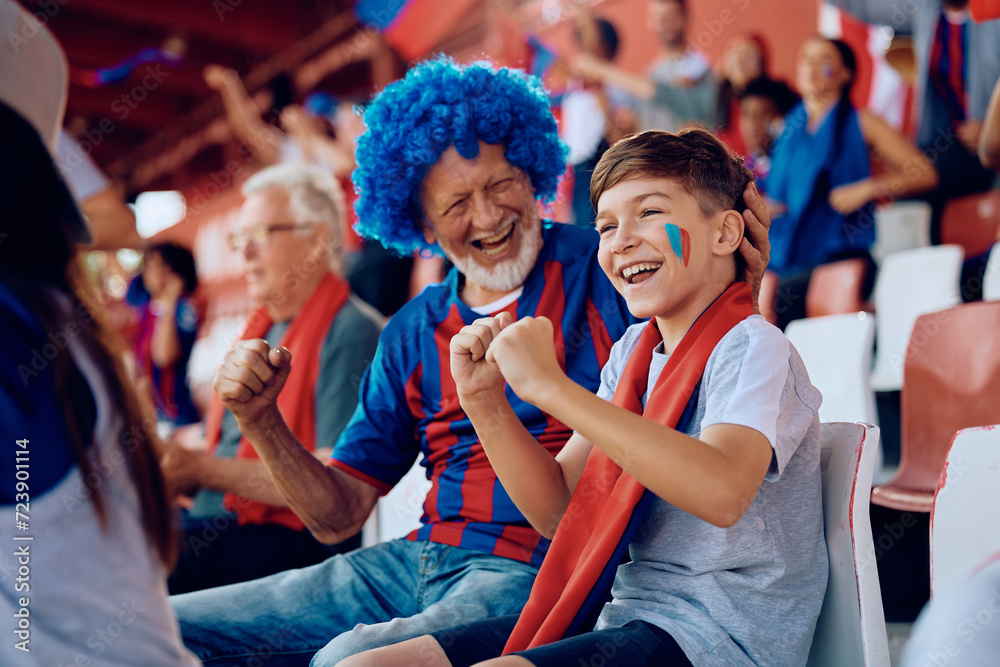 Wall mural happy kid watching sports match with his grandfather at stadium.