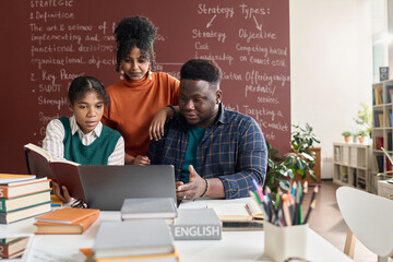 Front view portrait of three Black young people using laptop together while working on group project in school