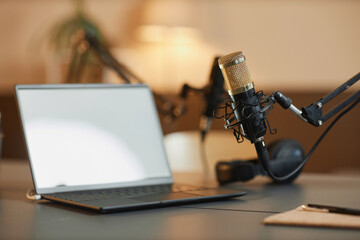 Close up shot of professional microphone with gold steel net and defocused white screen laptop on...
