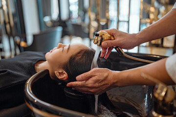 Asian woman lying down on salon washing bed getting hair washed in hair salon by stylist,...