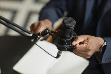 Top down view of unrecognizable male hand arranging studio microphone during online podcast