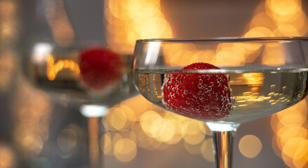 Close up of champagne in wineglasses with ripe strawberries with bubbles on background of golden blurred lights. Sparkling wine - obrazy, fototapety, plakaty