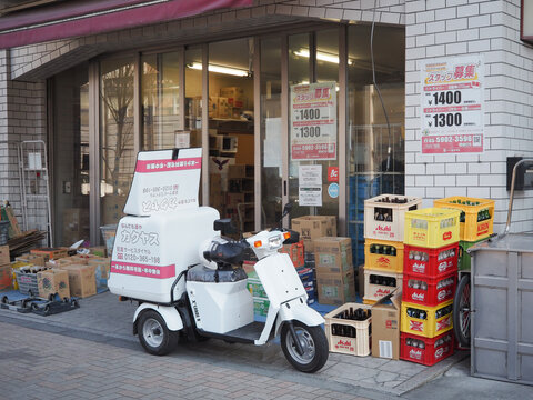 TOKYO, JAPAN - January 30, 2024: An X3 Loader electic delivery scooter and crates of empty beer bottles outside a Kakuyasu branch in Tokyo.