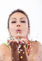 Woman's face with hands in front, blowing colorful confetti on a white background