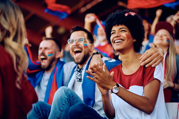Happy black sports fan and her friends applauding during match at stadium.
